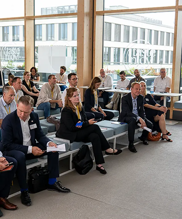 Mehrere Teilnehmer hören dem Referenten zu. Die Aufnahme zeigt die Teilnehmenden von vorne