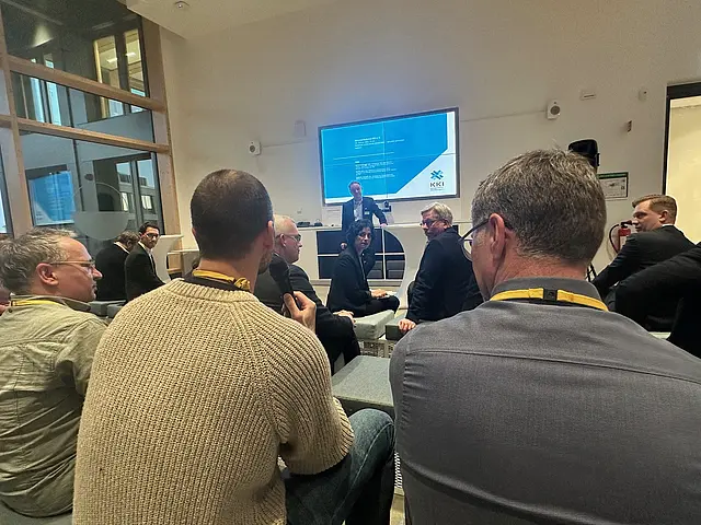 Mehrere Teilnehmer von hinten. Ein Mann hält das Mikro und stellt eine Frage